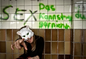 Frau mit Katzenmaske vor Wand mit Spruch
